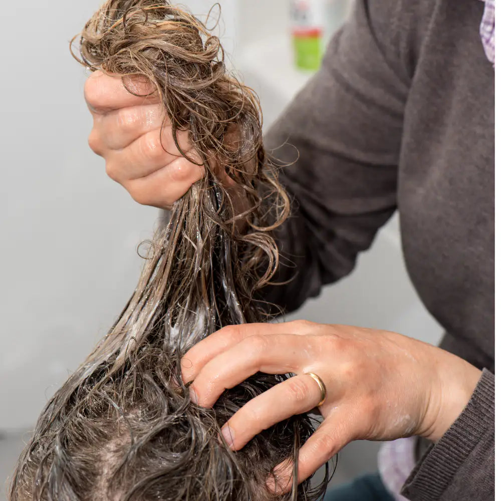 Mains d'une personne massant les cheveux d'une autre personne avec un shampooing anti-poux